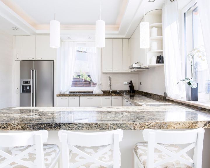 a kitchen with a marble counter top and white chairs.
